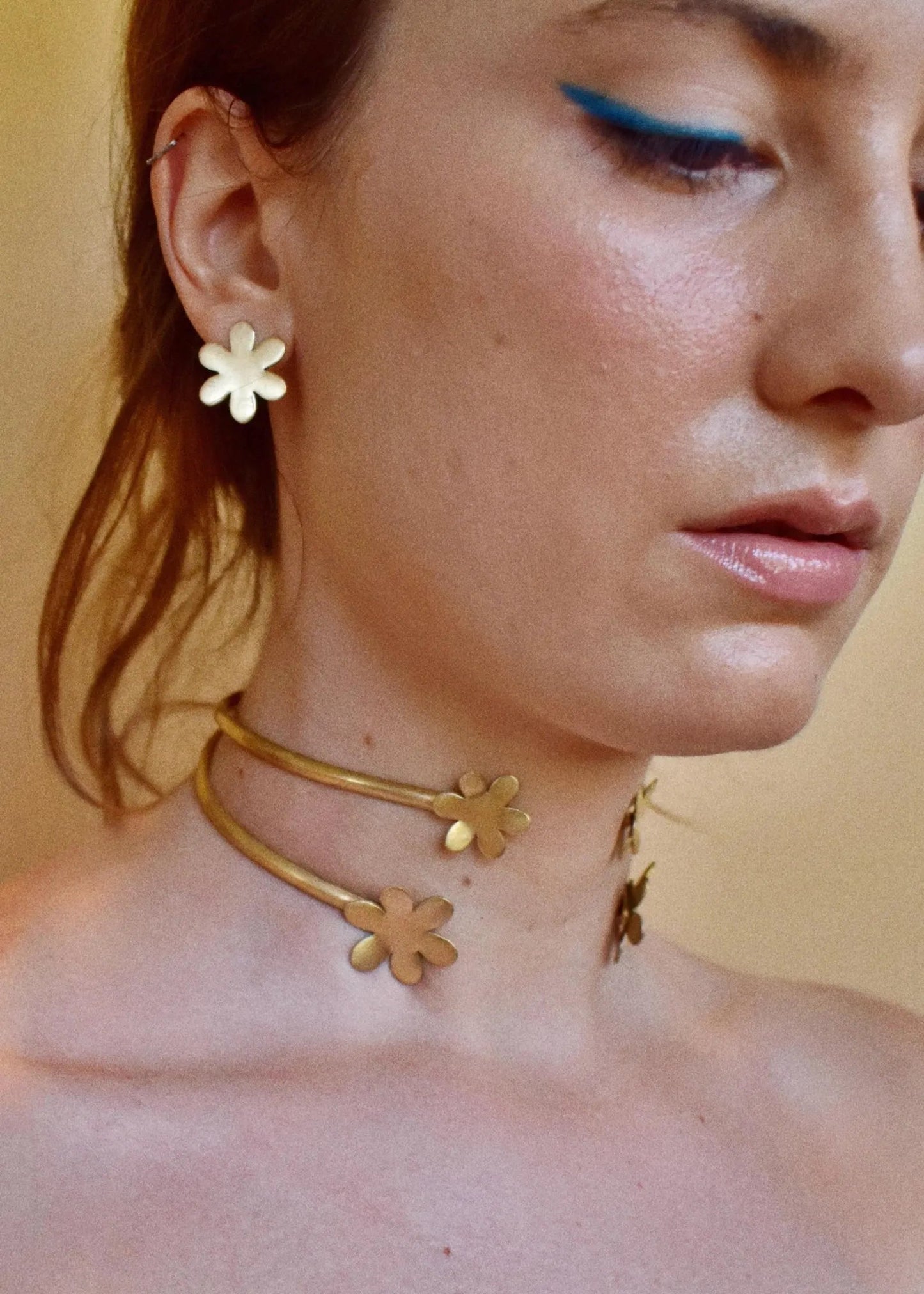 Close-up of a person wearing a gold floral necklace with a neutral background
