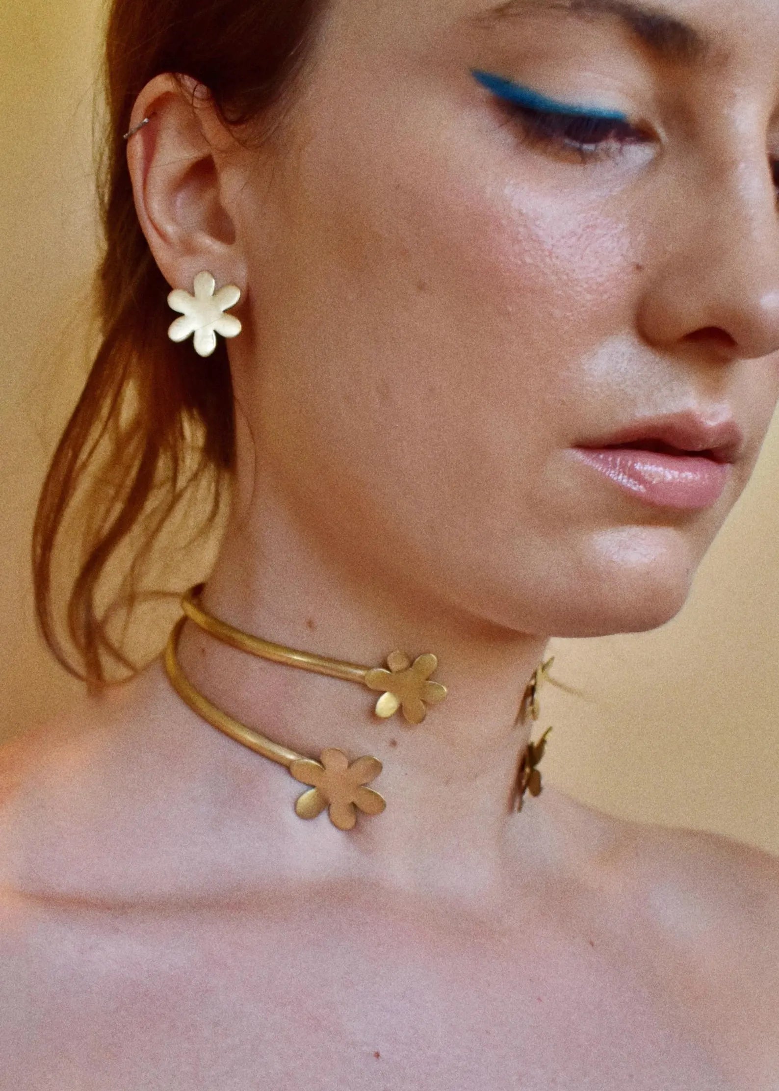 Close-up of a person wearing a gold floral necklace with a neutral background