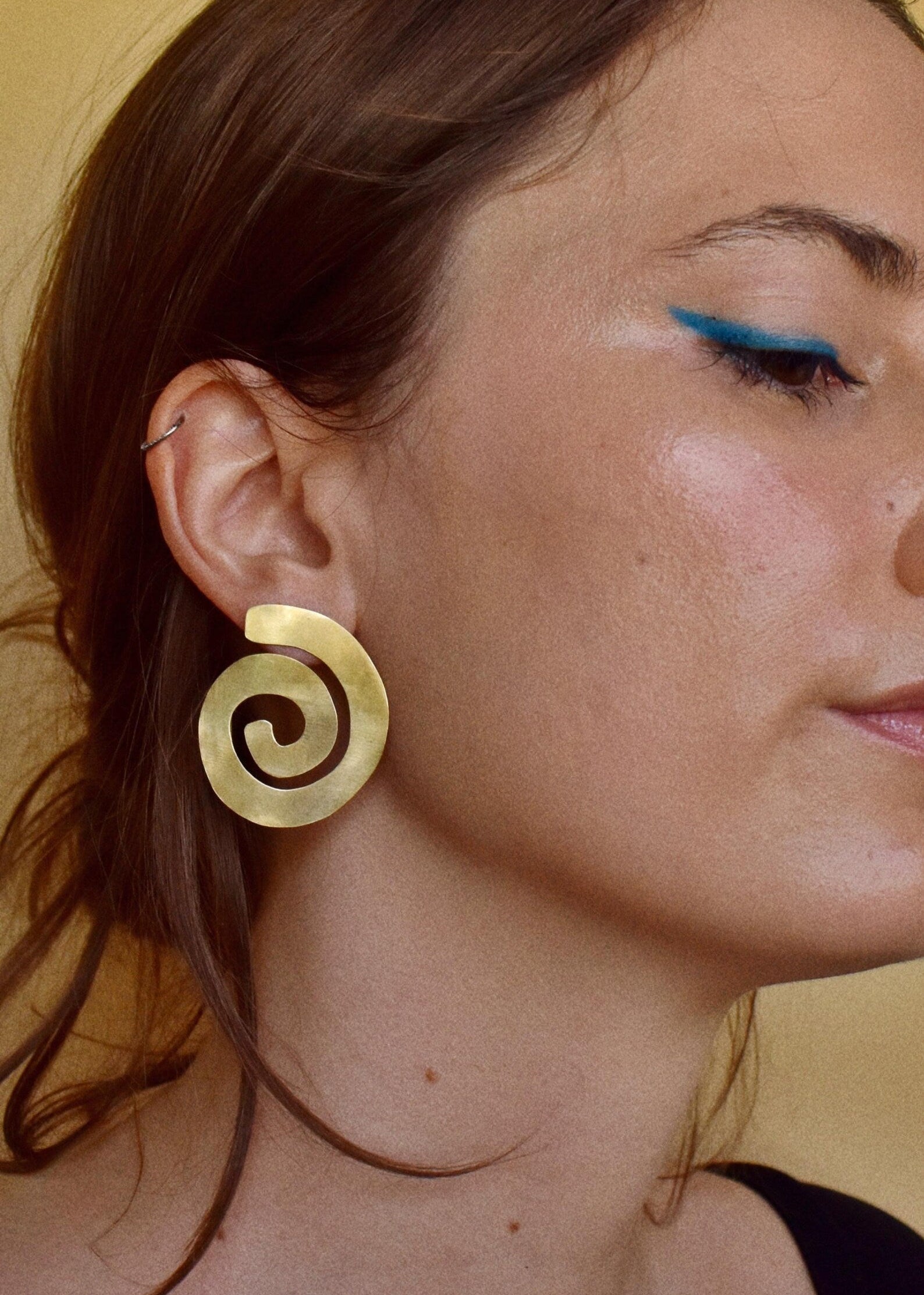 Close-up of a woman wearing a gold spiral earring against a neutral background