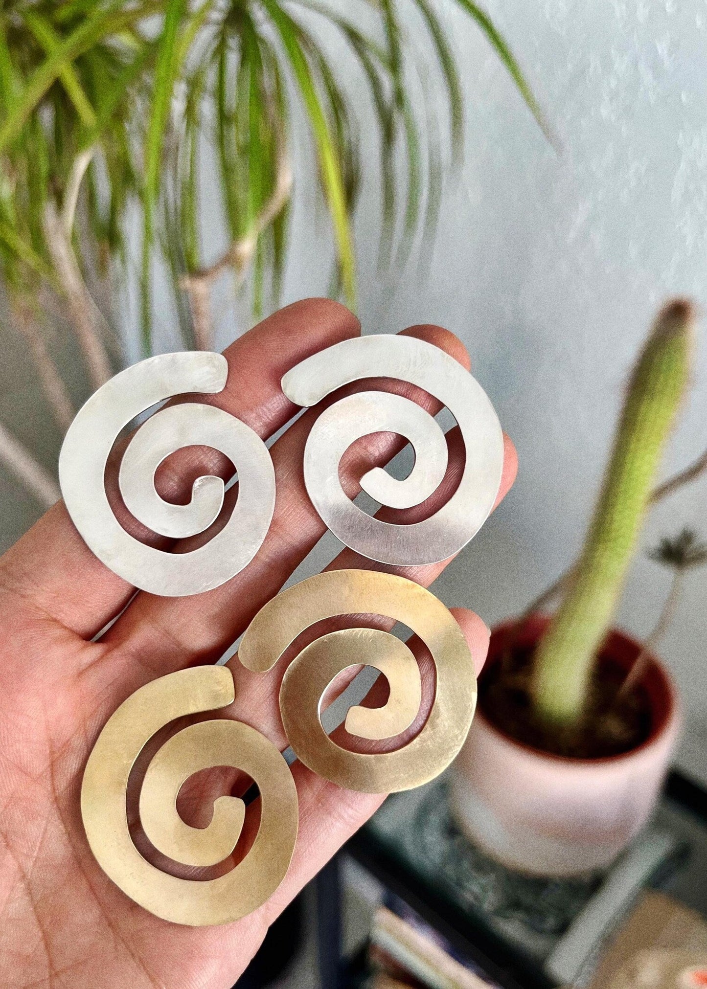 Hand holding two spiral-shaped earrings, one silver and one gold.