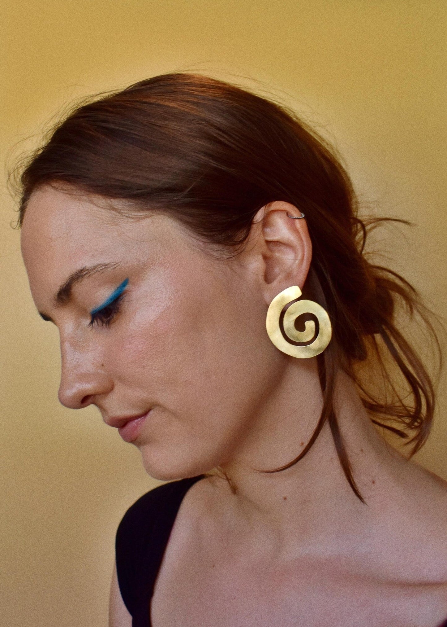 Woman wearing a gold spiral earring against a beige background