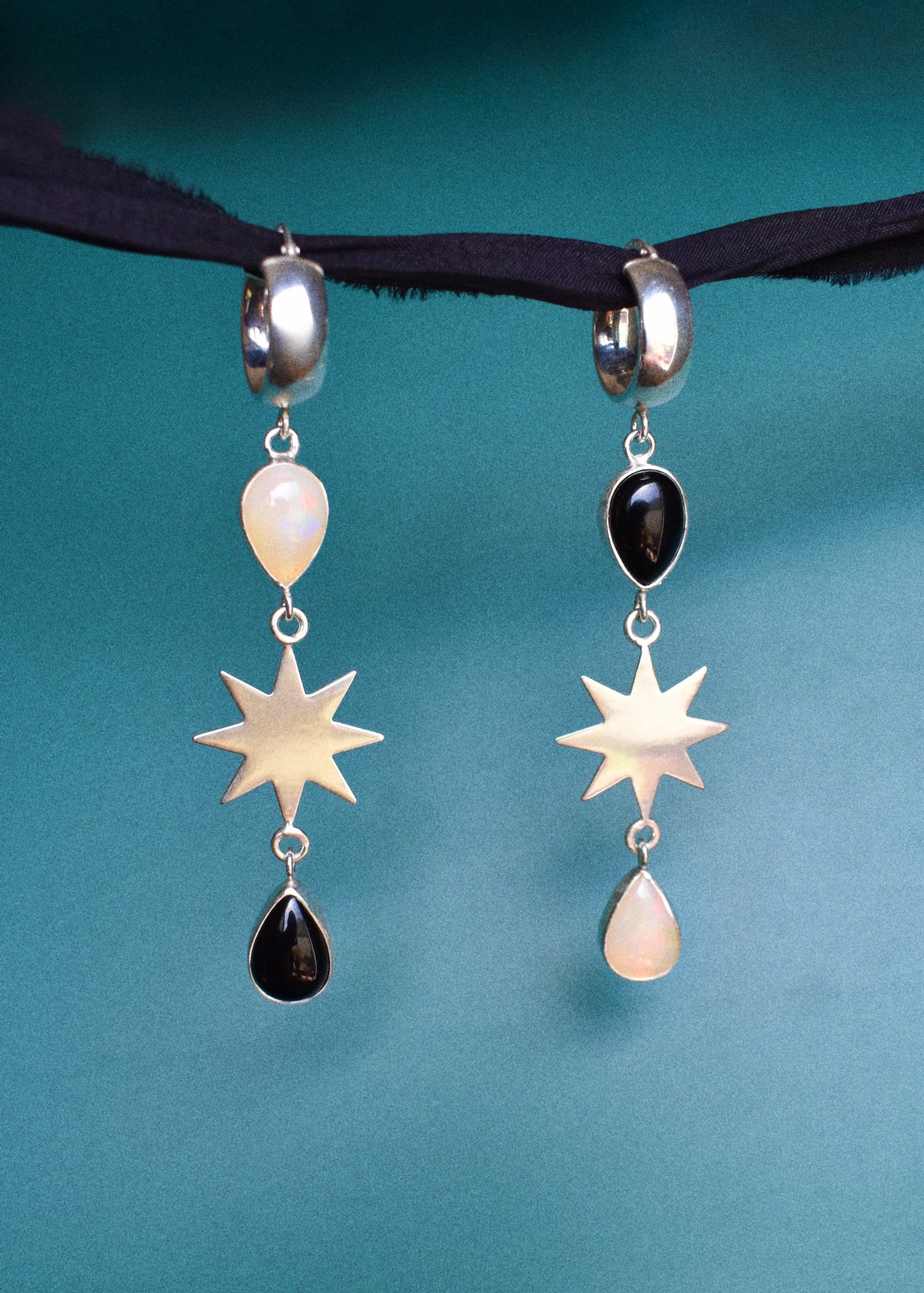Pair of earrings with star and teardrop opal and onyx designs on a teal background