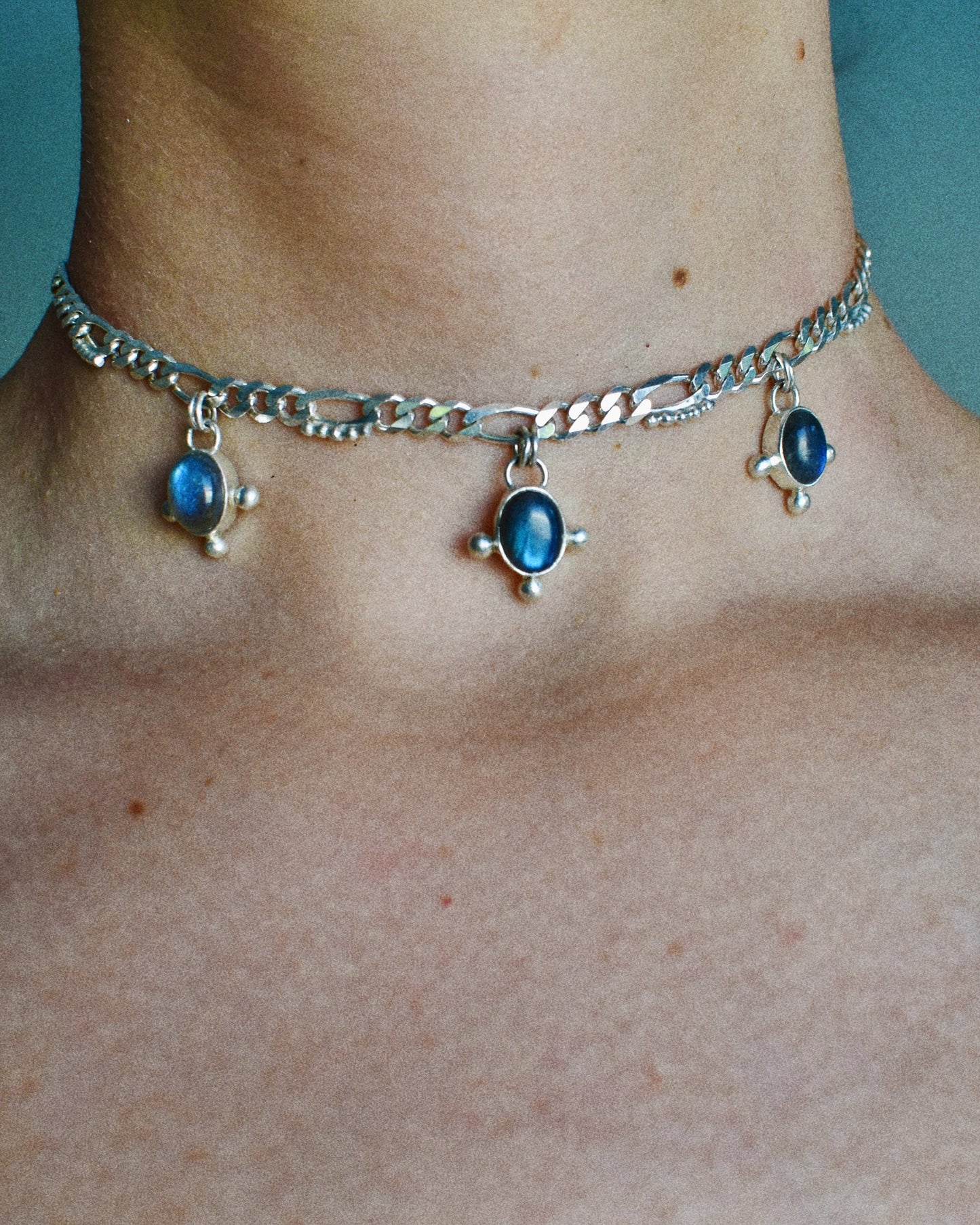 Silver choker necklace with blue labradorite stones on a person's neck.