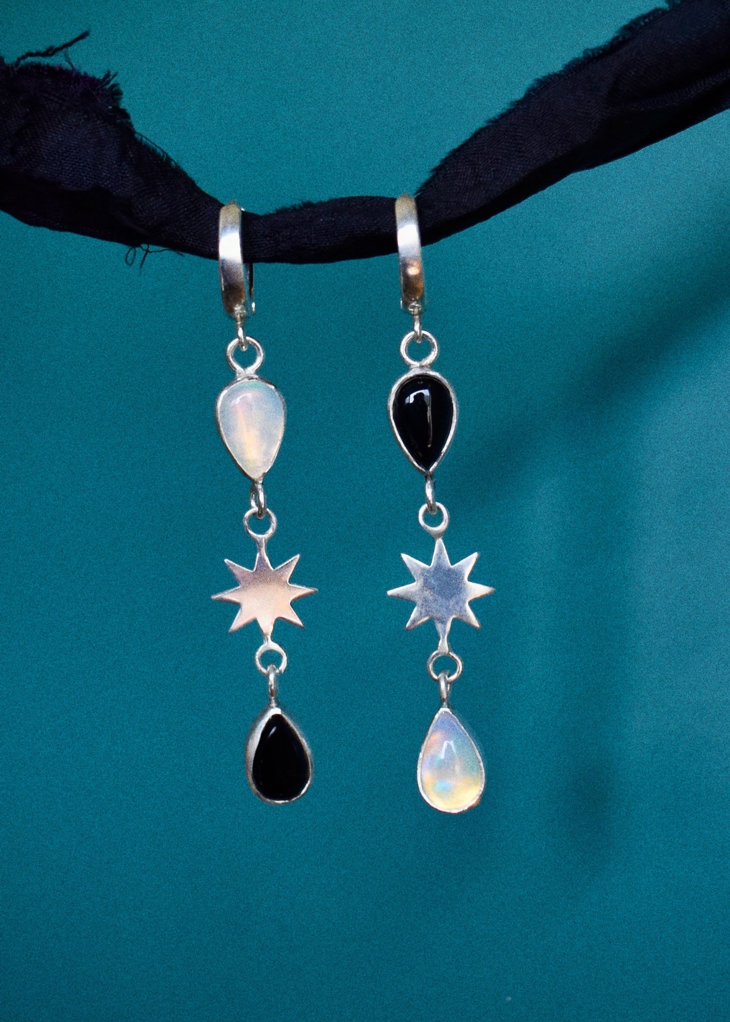 Pair of earrings with star and teardrop designs with opal and onyx on a teal background