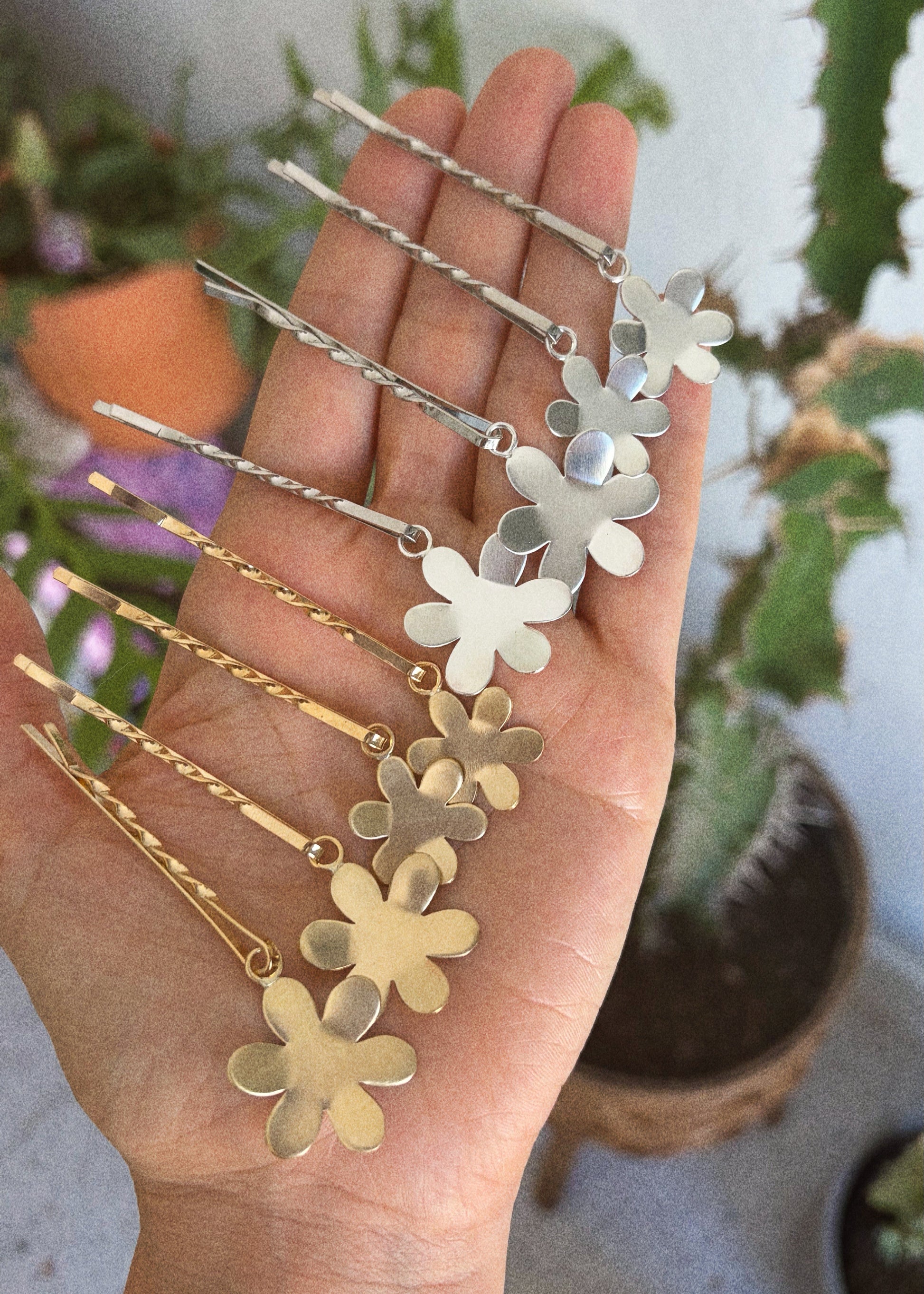 Hand holding gold and silver floral hairpins with plants in the background